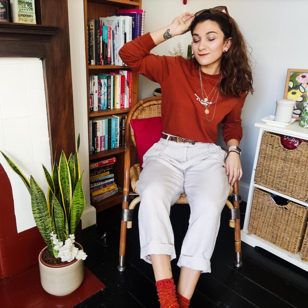 Safia seated in Red jumper and white linen trousers